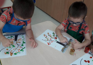 dwaj chłopcy malują paluszkami listki jesiennego drzewa