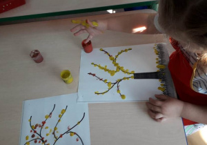 dziewczynka maluje paluszkami listki jesiennego drzewa