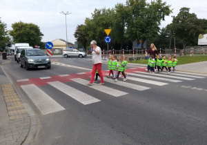 dzieci w kamizelkach odblaskowych parami przechodzą przez ulicę