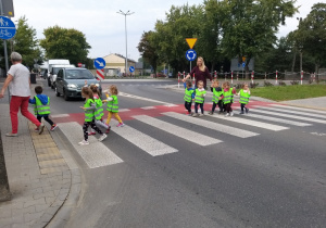 dzieci w kamizelkach odblaskowych parami przechodzą przez ulicę