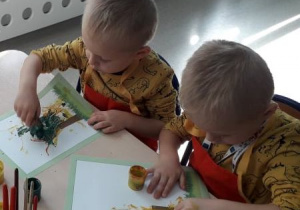 dwaj chłopcy szyszkami malują konary drzewa