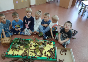 Dzieci prezentują pejzaż jesienny ułożony z kasztanów, żołędzi, liści i patyków.