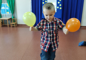 Chłopiec idzie po ławeczce z drewna trzymając w dłoniach balony