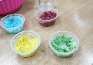 dzieci wsypują cukier wymieszany z olejem z pestek winogron do pojemniczków a następnie zabarwiają go barwnikami spożywczymi