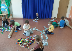 Dzieci układają pejzaż z kolorowych nakrętek od butelek PET