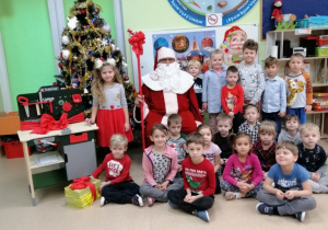 Dzieci z Mikołajem przy choince cieszą się prezentami.