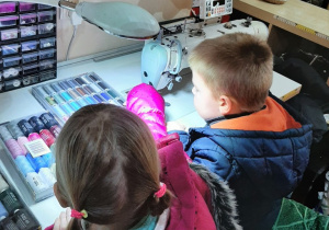 Dziewczynka z chłopcem oglądają kolorowe guziki i szpulki z nićmi.
