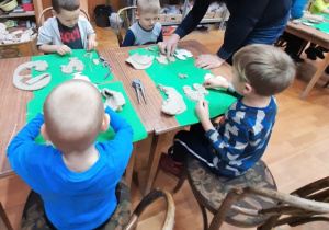 Instruktor pokazuje chłopcom jak wyciąć i ozdobić gliniane koguciki