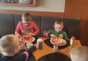Dzieci jedzą wykonaną przez siebie pizzę