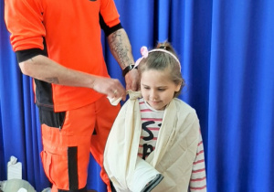 Ratownik medyczny wkłada dziewczynce rękę w stabilizator ortopedyczny - temblak