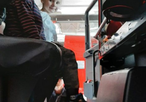 Dziewczynka z chłopcem siedzą w wozie strażackim.