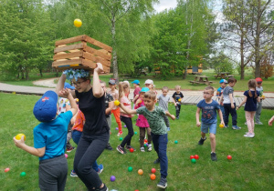 Przedszkolaki próbują wrzucić piłki do ruchomej skrzynki