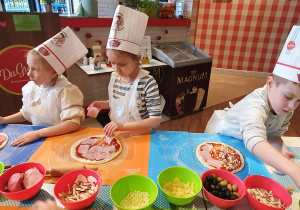 Troje dzieci układa składniki na cieście do pizzy.