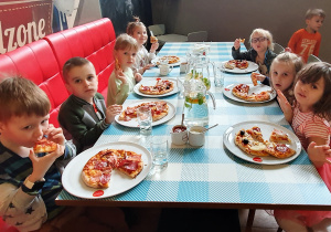 Dzieci jedzą pizzę.