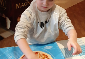 Chłopiec układa dodatki na pizzy.