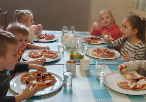 Przedszkolaki jedzą własnoręcznie przygotowane pizze.