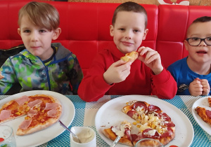 Chłopcy jedzą własnoręcznie przygotowaną pizzę.