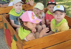 Przedszkolaki siedzą w wagonikach zbudowanych ze skrzyń po jabłkach.