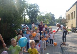 Przedszkolaki spacerują z balonikami na placu szkolnym.