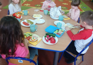 Dzieci kroją warzywa oraz smarują chleb masłem