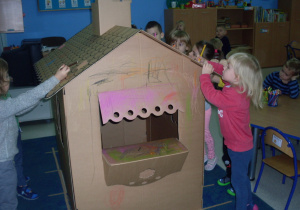 Dzieci kolorują tekturowy domek.