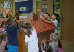 Dzieci koloruja tekturowy domek.