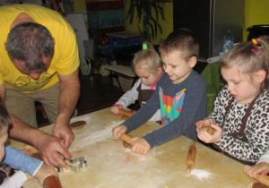 Dzieci wykrawają foremkami pierniczki z ciasta.