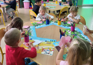Dzieci kolorują na czerwono papierowe serduszka.