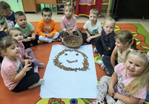 Dzieci prezentują uśmiechniętą buźkę-symbol radości,wykonaną z żołędzi.