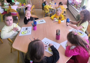 Przedszkolaki kolorują uśmiechnięte buźki.