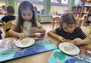 Dziewczynki wkładają wykałaczki–kolce jeża w masę solną.