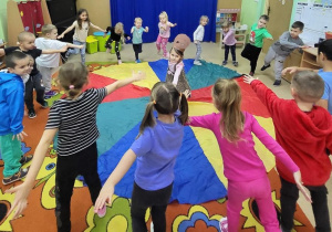 Dzieci uczestniczą w zabawie muzyczno-ruchowej z chustą animacyjną.