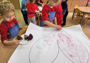 Dziewczynka z chłopcem stempluje za pomocą buraka serca.