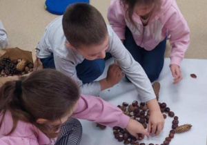 Dzieci układają misia z darów natury.