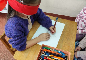 Dziewczynka z zakrytymi oczami rysuje misia według wskazówek.