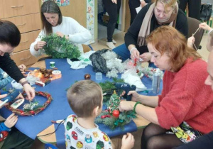 Rodzice wspólnie z dziećmi robią stroiki świąteczne.