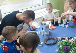 Rodzice wspólnie z dziećmi robią stroiki świąteczne.