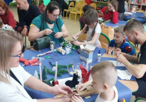 Rodzice wspólnie z dziećmi robią stroiki świąteczne.