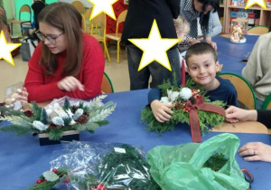 Rodzice wspólnie z dziećmi robią stroiki świąteczne.