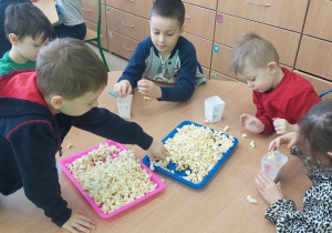 Żabki wkładają popcorn do własnoręcznie zrobionych pudełek