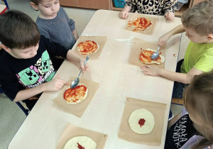 Dzieci smarują placek sosem pomidorowym.