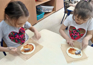 Dzieci smarują placek sosem pomidorowym.