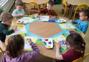 Dzieci malują obrazek przedstawiający czapkę farbami z użyciem patyczków higienicznych.