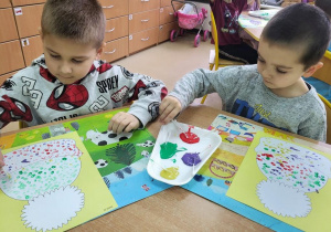 Chłopcy malują obrazek przedstawiający czapkę farbami z użyciem patyczków higienicznych.