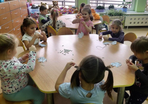 Dzieci nawlekają kawałki słomek na sznurek tworząc trąbę słonia.