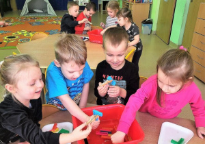 Dzieci łowią z wody plastikowe nakrętki z użyciem klamerek do bielizny.