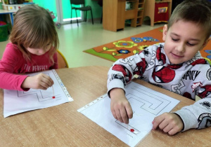 Dziewczynka z chłopcem prowadzą kroplę wody po wyznaczonym torze za pomocą wykałaczki.