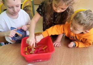 Dzieci łowią z wody plastikowe nakrętki z użyciem klamerek do bielizny.