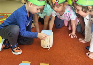 Chłopiec z użyciem lampki zgaduje, jaki owad ukrył się w słoiczku.