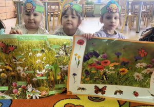 Dziewczynki prezentują plansze z owadami żyjącymi na łące.